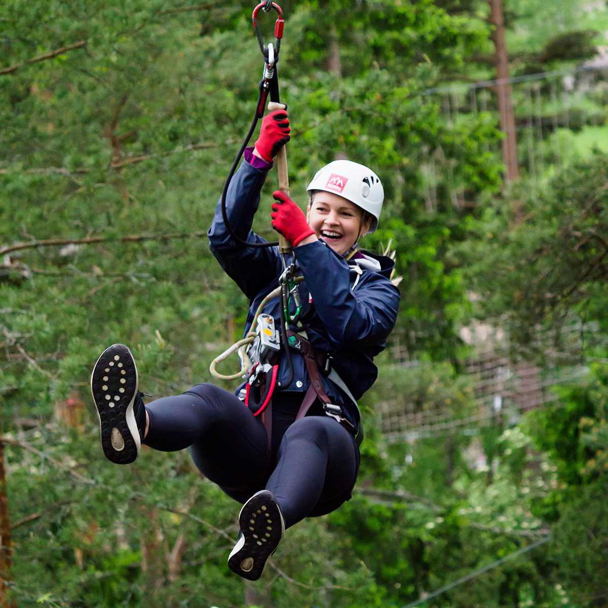Nuori nainen liitää tarzan-hypyssä ”liaanilla” puusta puuhun.